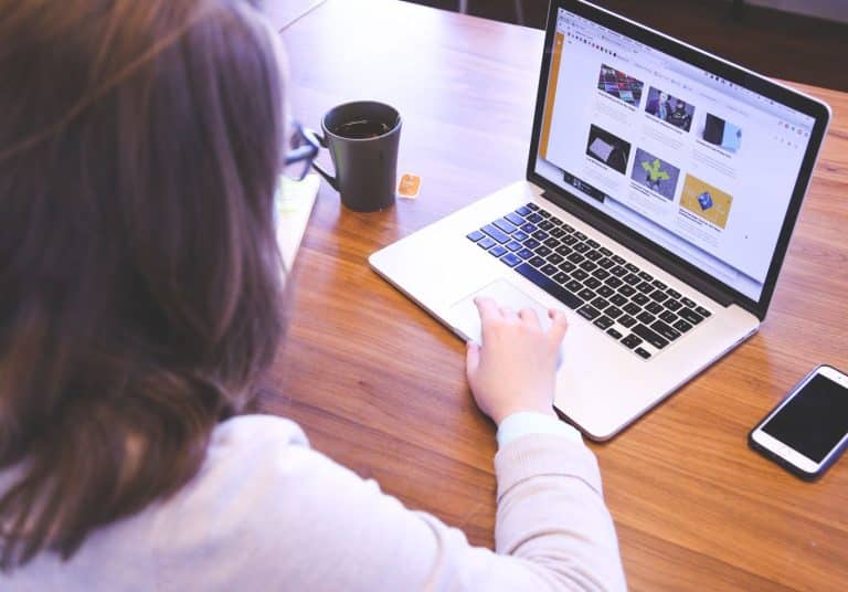Femme consultant un site internet sur un ordinateur portable posé sur une table en bois, à côté d'un mug et d'un smartphone